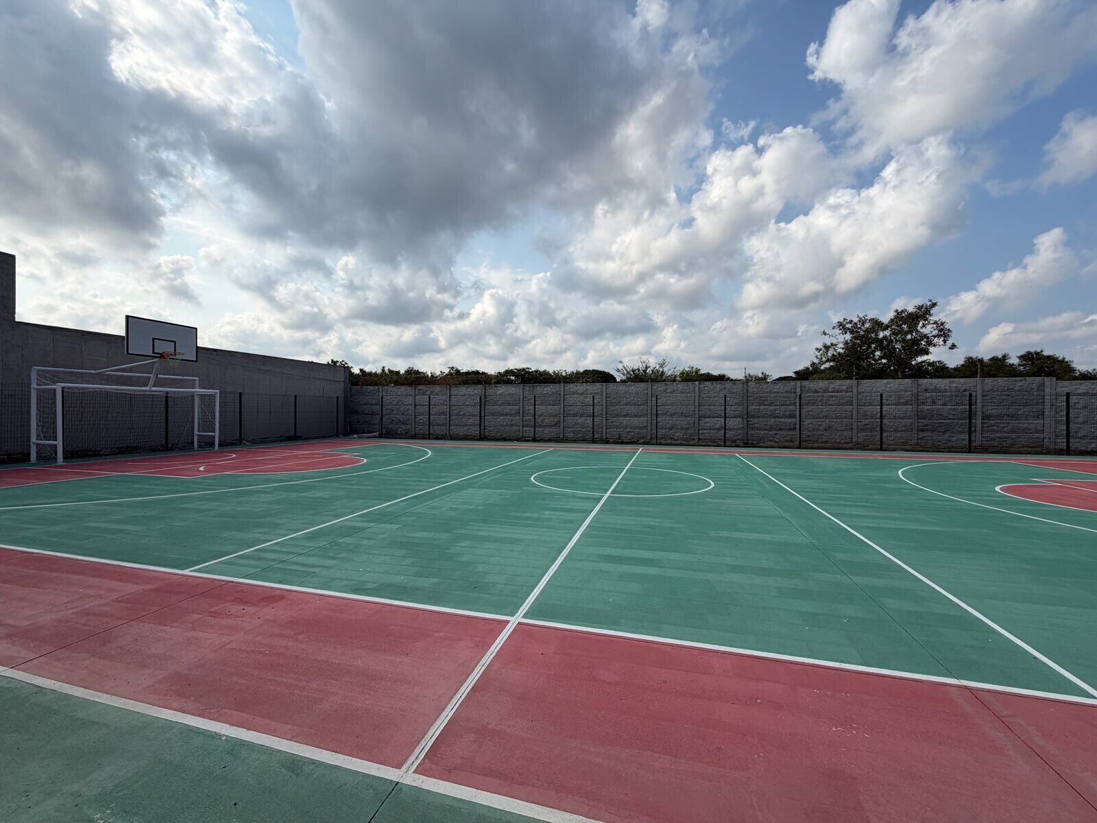 Ein Basketballplatz im Freien mit Korb, umgeben von einer Steinmauer und Bäumen.