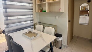 A modern dining area with a white marble table, grey chairs, and a white cabinet with shelves above.