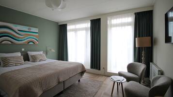Habitación de hotel con cama, dos sillones, una mesita, una lámpara y un cuadro en la pared.