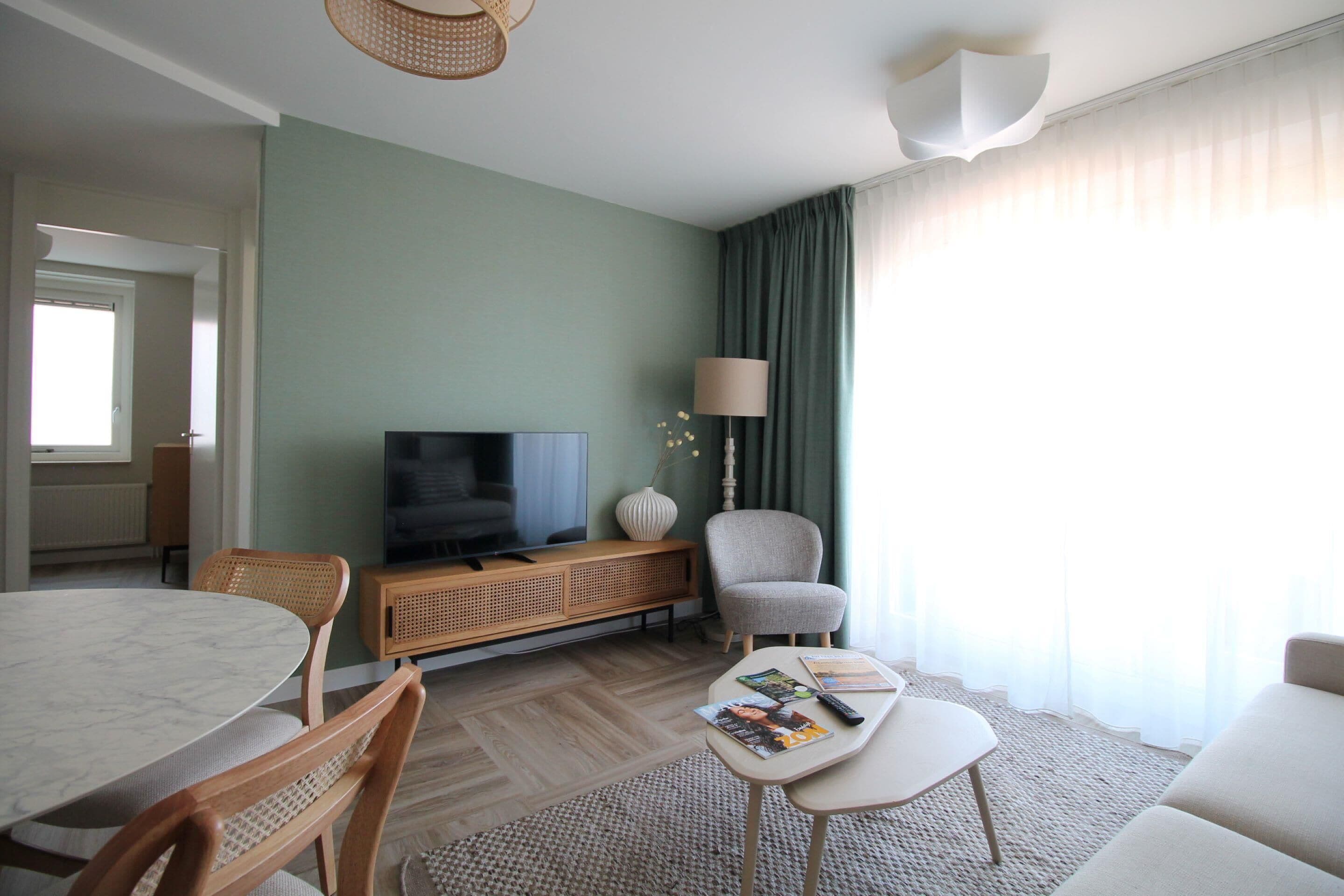 A modern living room with a television, seating, and a dining area.