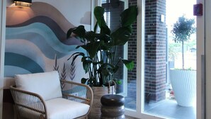 A reception area with a wicker chair, a large potted plant, and a wall mural. - Best Western Beach Hotel Bergen Aan Zee (Bergen aan Zee)