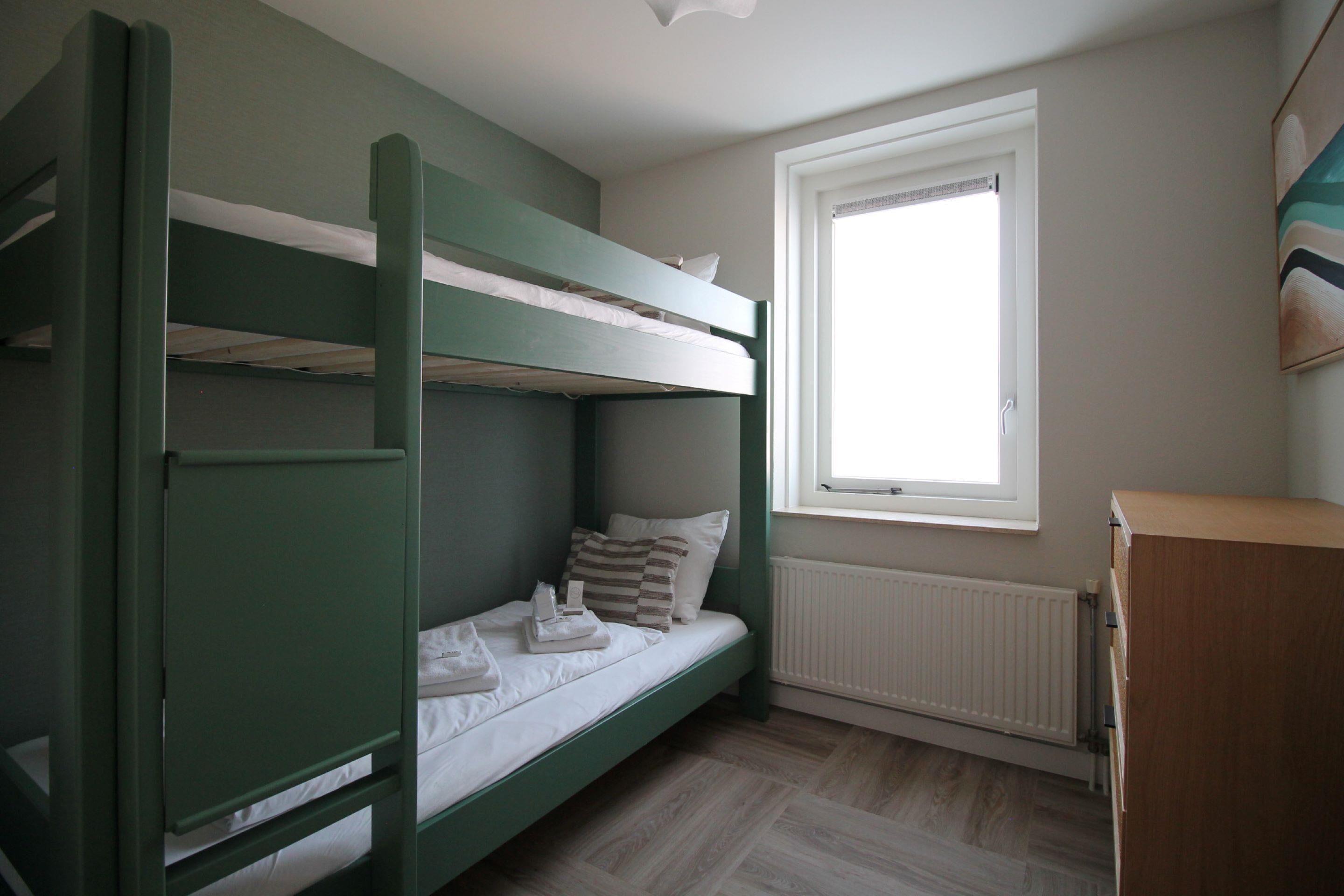A bunk bed room with a window, radiator, and a wooden cabinet.