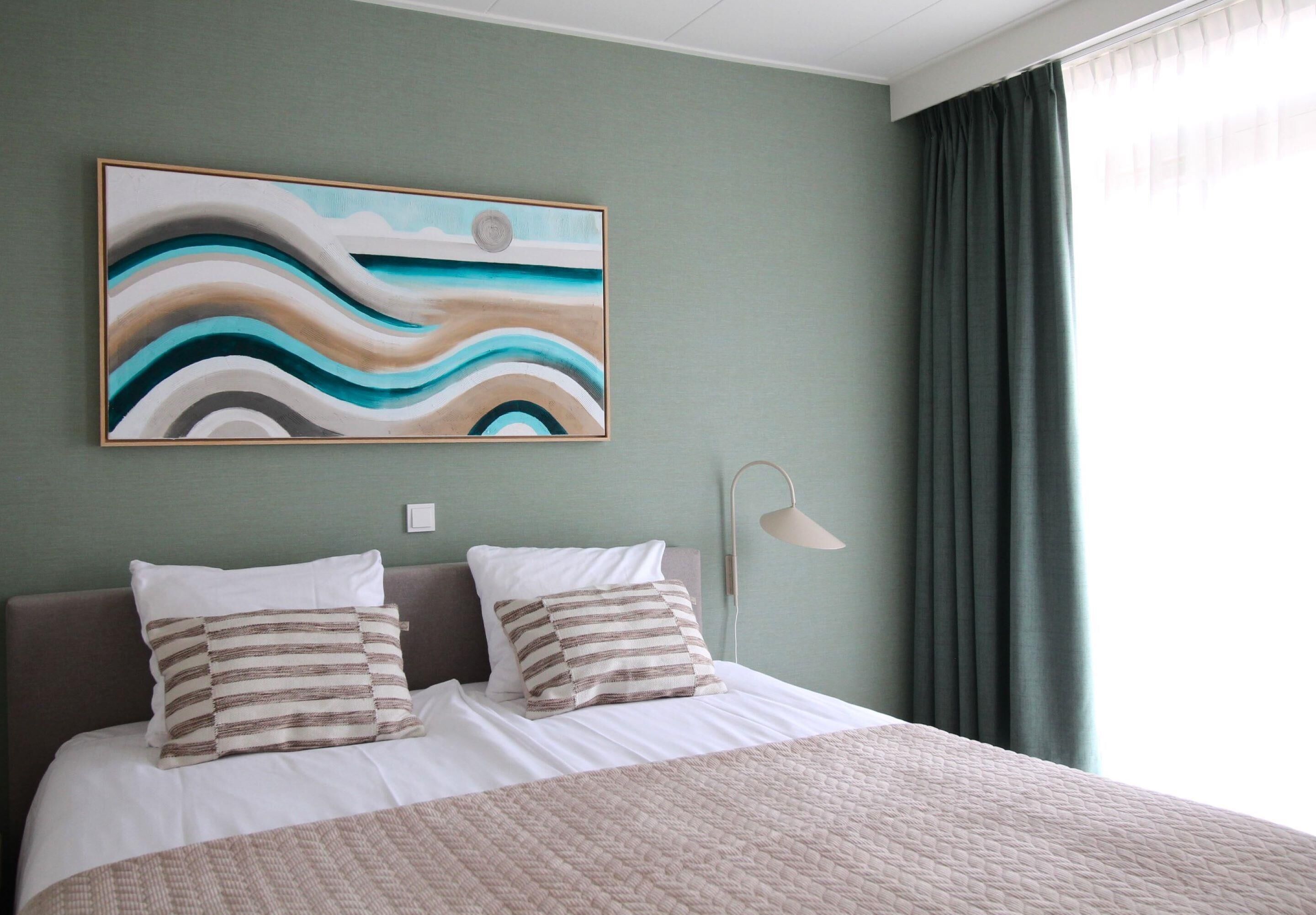 Una cama bien hecha con almohadas a rayas, un cuadro abstracto grande en la pared y una lámpara de noche.