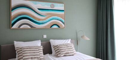 Una cama bien hecha con almohadas a rayas, un cuadro abstracto grande en la pared y una lámpara de noche.