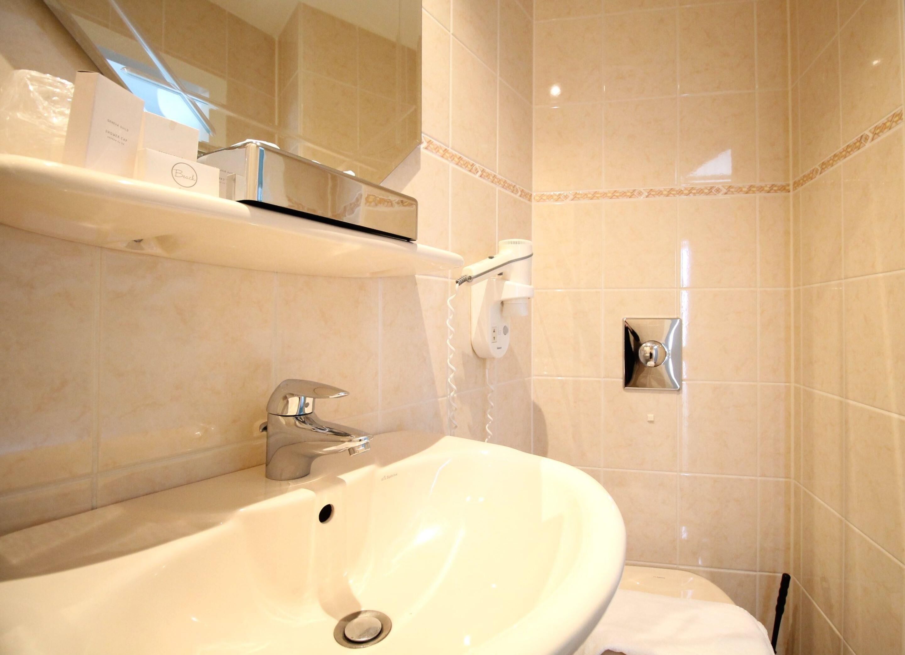 A bathroom with a white sink, a mirror, a hairdryer, and a shelf with toiletries.