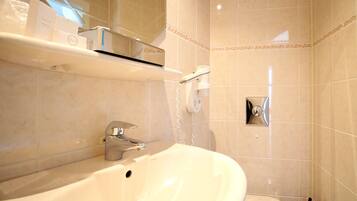 A bathroom with a white sink, a mirror, a hairdryer, and a shelf with toiletries.