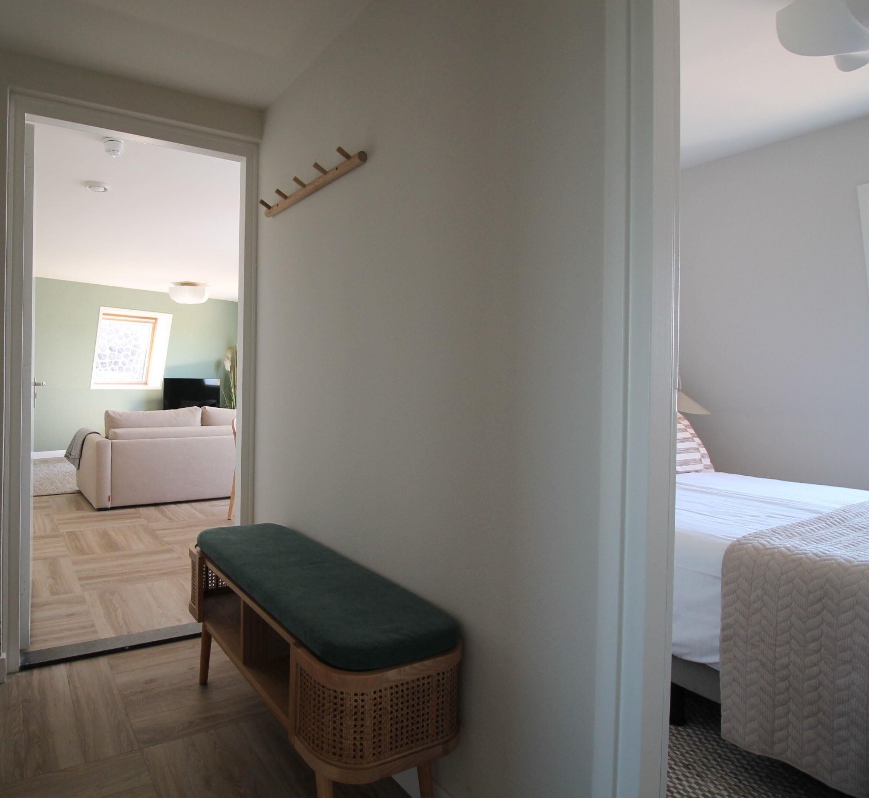 A bedroom with a bed, a bench, and a door leading to another room.