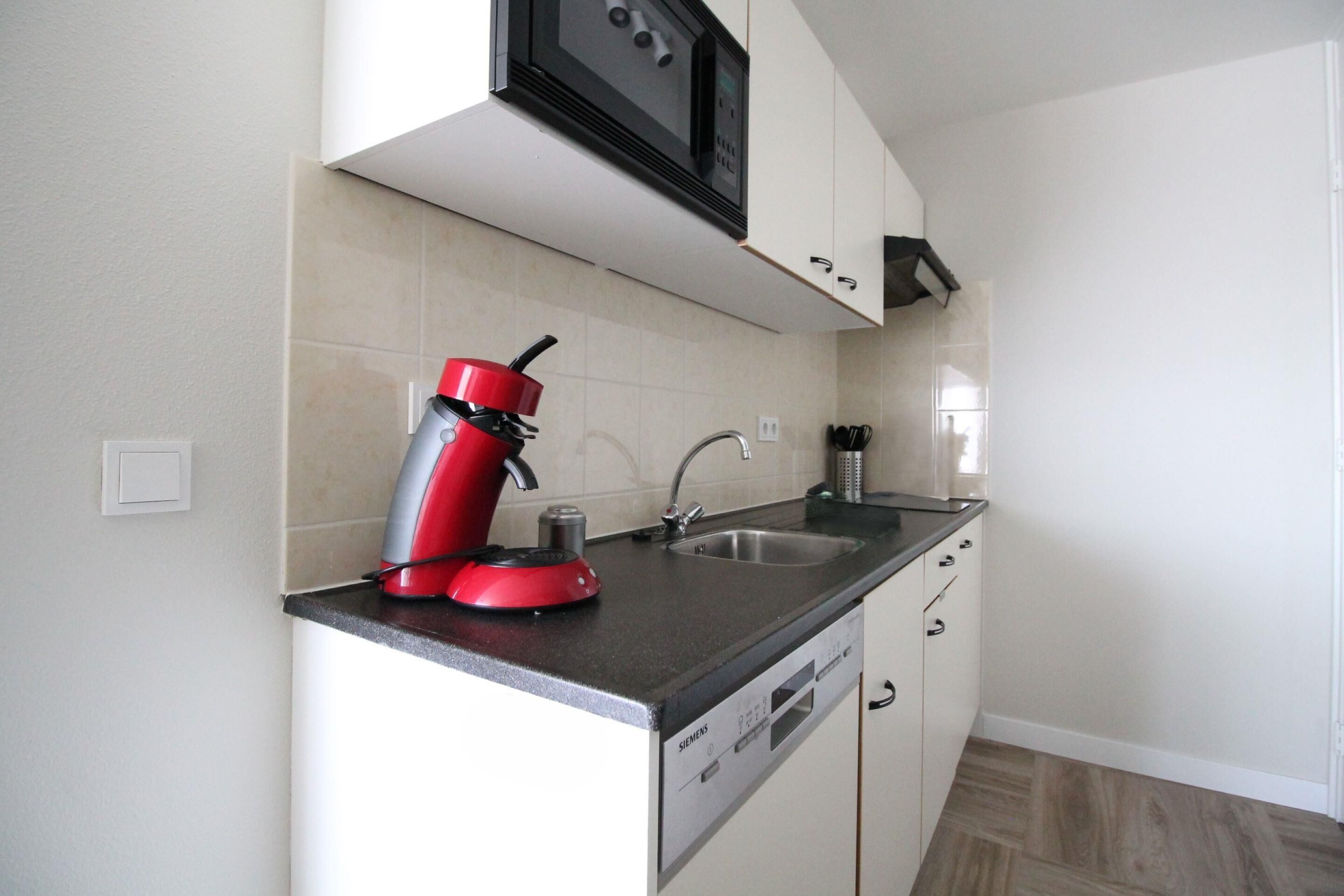 A kitchen with a red coffee maker, a sink, and a dishwasher.