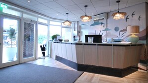 A modern reception area with a wooden counter, pendant lighting, and a mural of birds and clouds on the wall. - Best Western Beach Hotel Bergen Aan Zee (Bergen aan Zee)