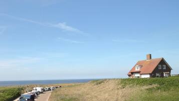 A coastal house with a long driveway lined with parked vehicles, overlooking the sea.