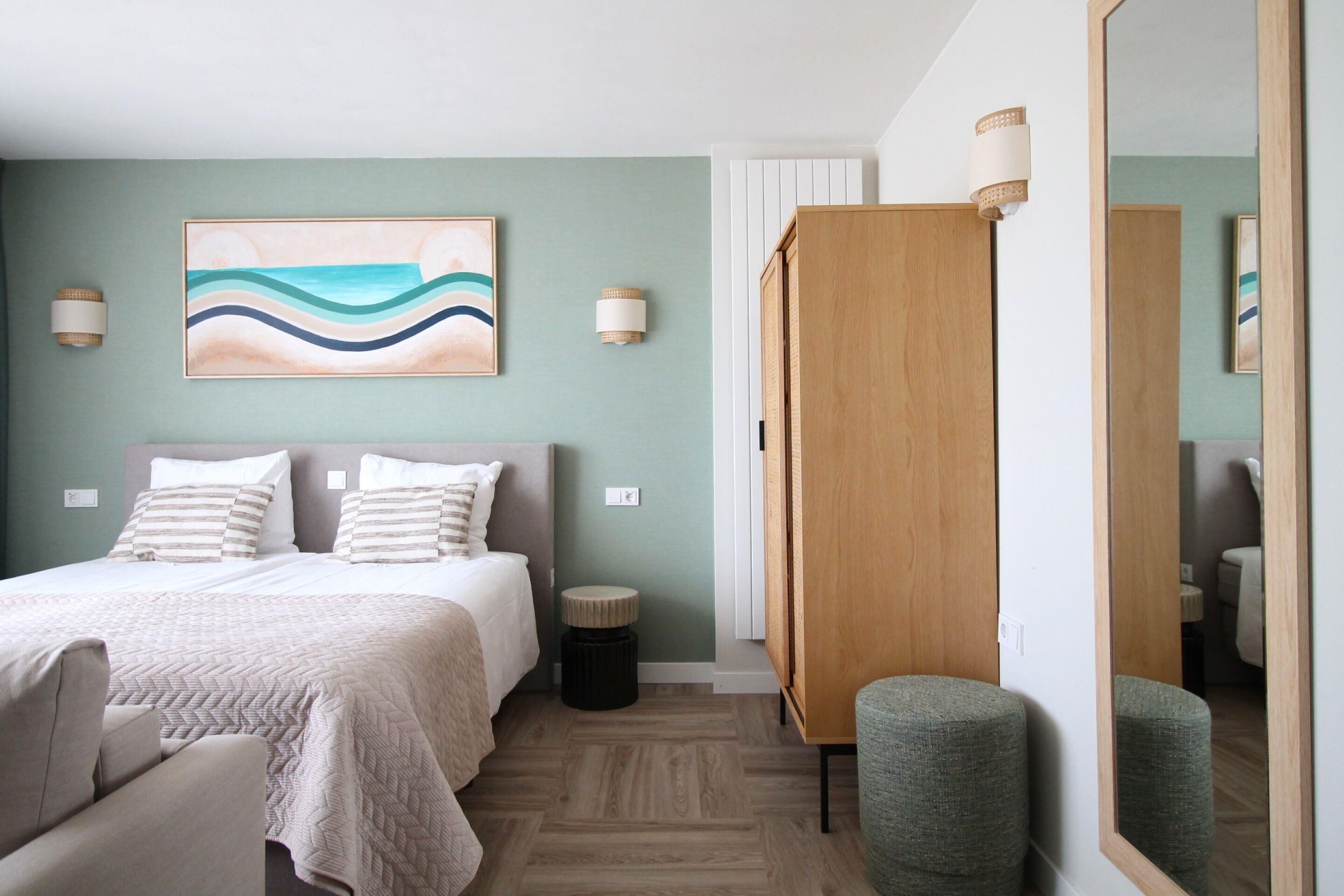 A hotel room with a bed, bedside tables, a mirror, a wall-mounted artwork, and a wooden wardrobe.