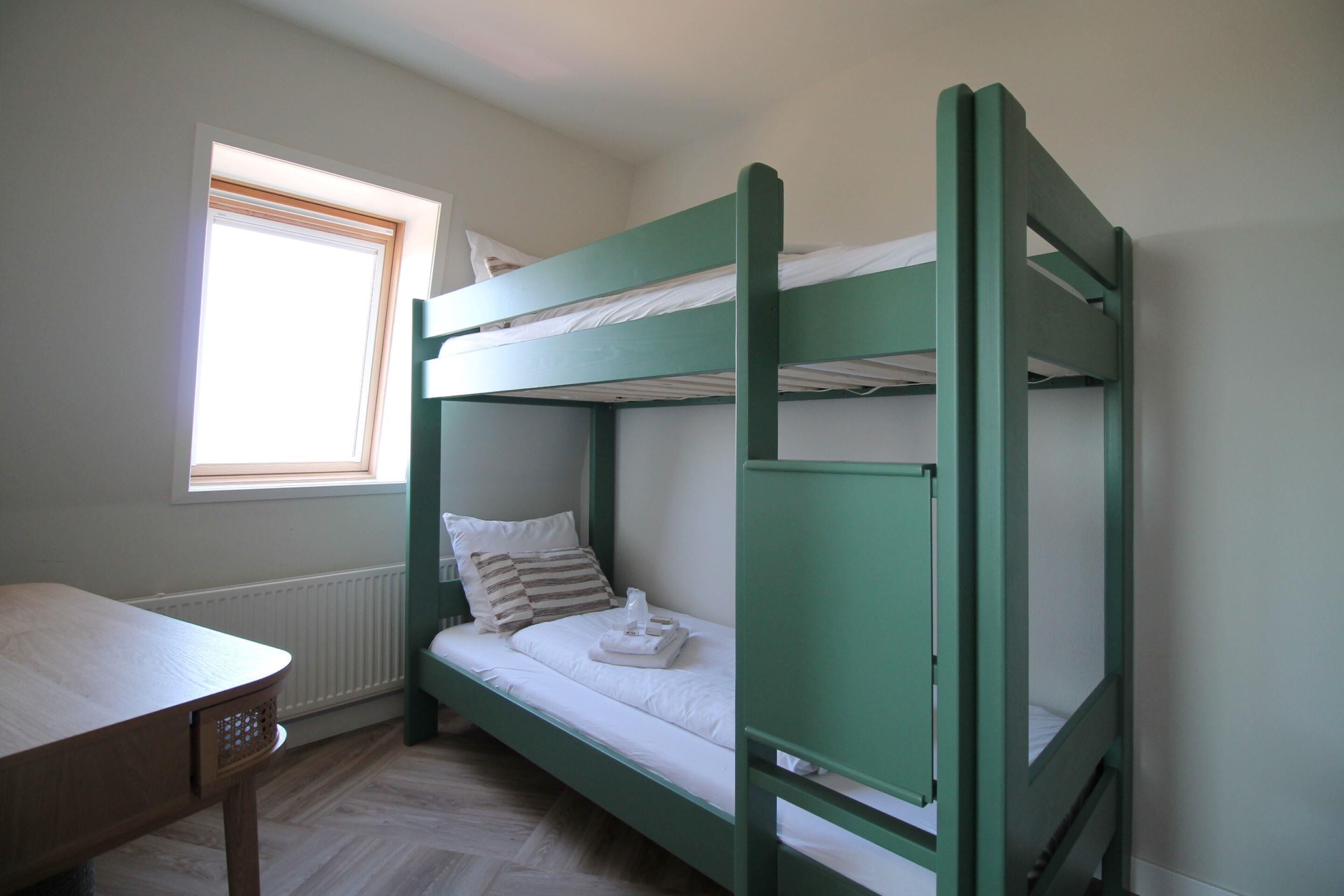 A bunk bed room with a window, a wooden table, and a radiator.