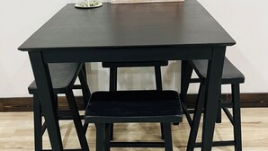 Een donker houten tafel met een bankje, een decoratief bord met de tekst 'STAY AWAY' en een klein glazen object op de tafel.
