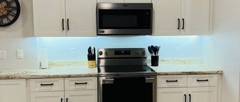 Una cocina con armarios blancos, microondas, horno y encimera de mármol.