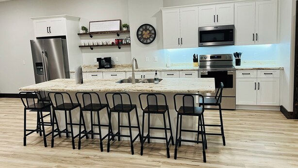 Een moderne keuken met een centraal eiland, barstoelen, roestvrijstalen apparatuur en witte kastjes.