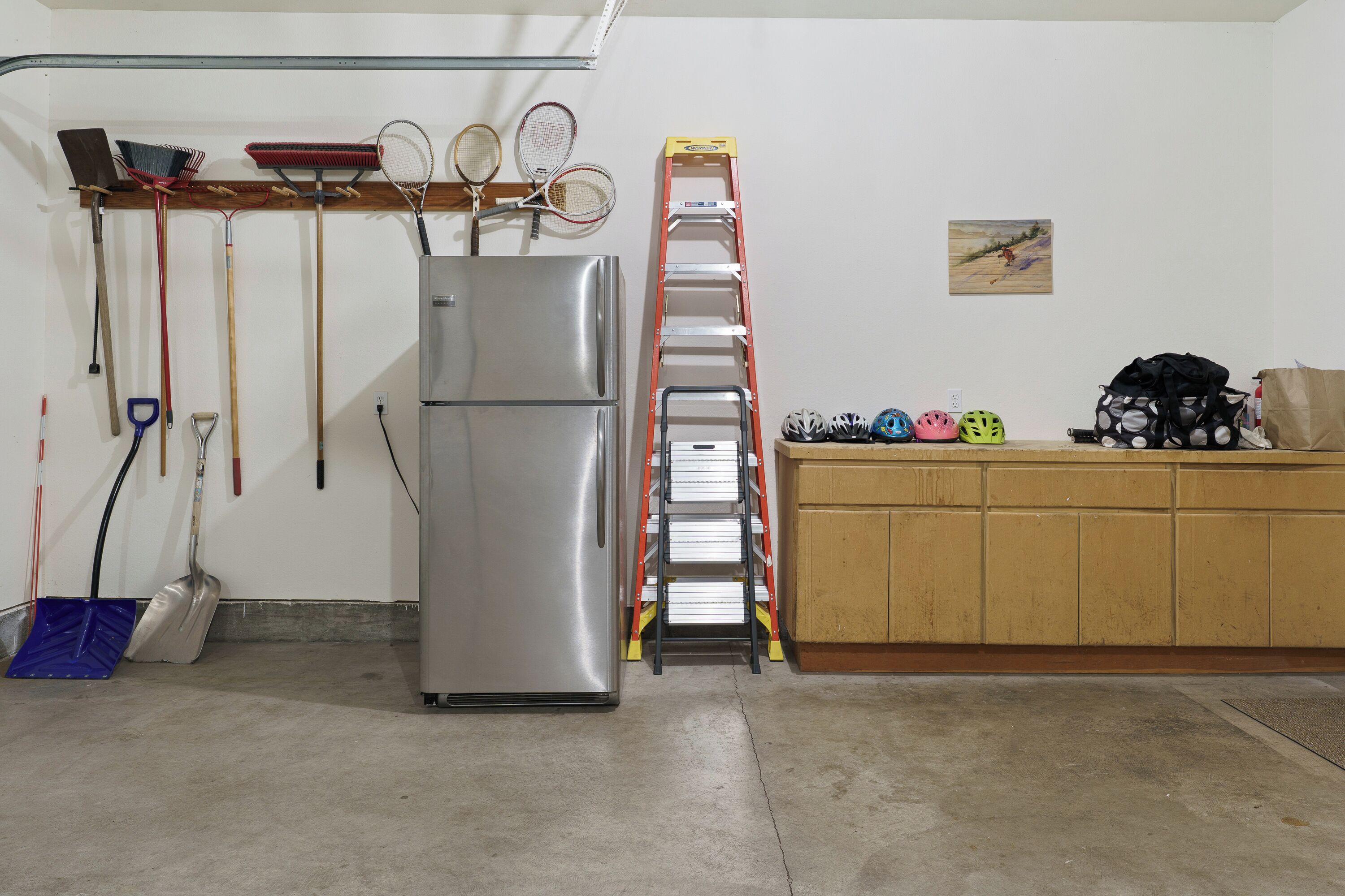 A kitchen with a stainless steel refrigerator, a wooden countertop, and various cleaning tools hanging on the wall.