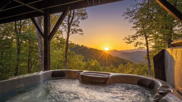 A hot tub with a view of a sunset over a forested mountain range.