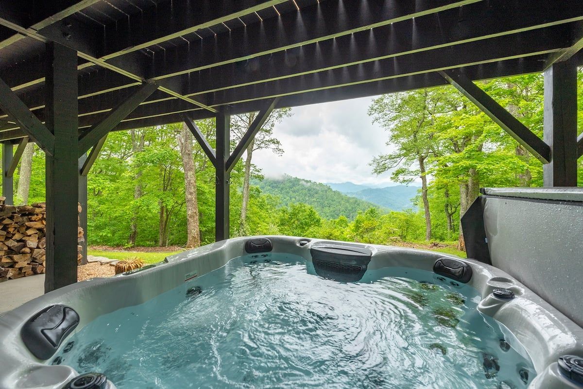 Een hottub onder een pergola met uitzicht op een bebost berglandschap.