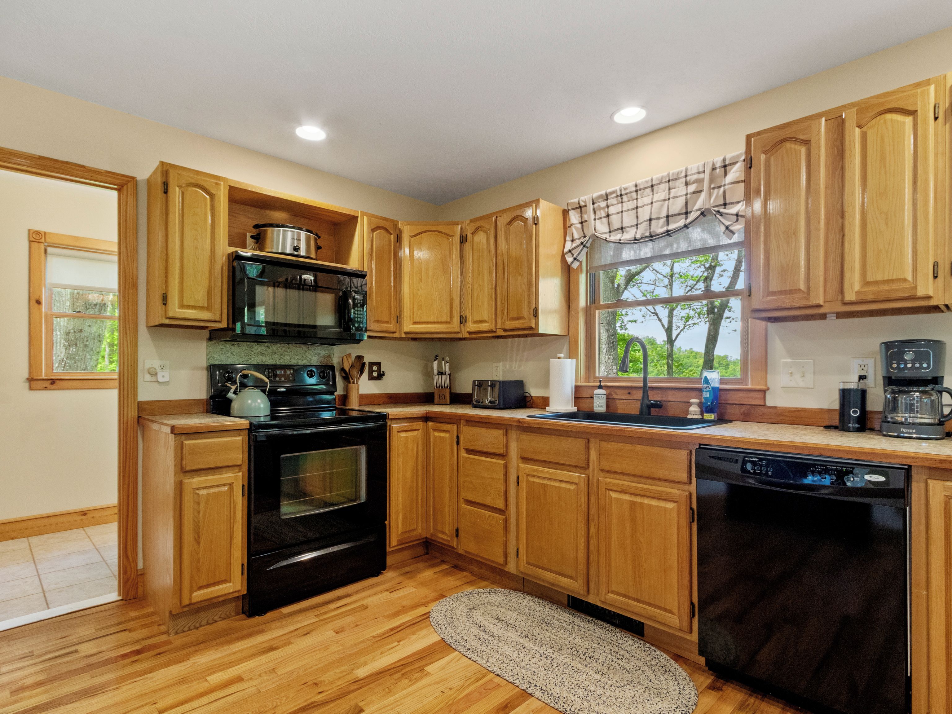 A kitchen with wooden cabinets, a stove, a microwave, a dishwasher, and a window with a view of trees.