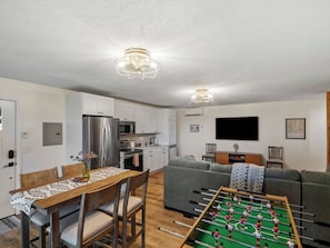Una cocina moderna con mesa de fútbol, un comedor con mesa y sillas, y una sala de estar con sofá y televisor.