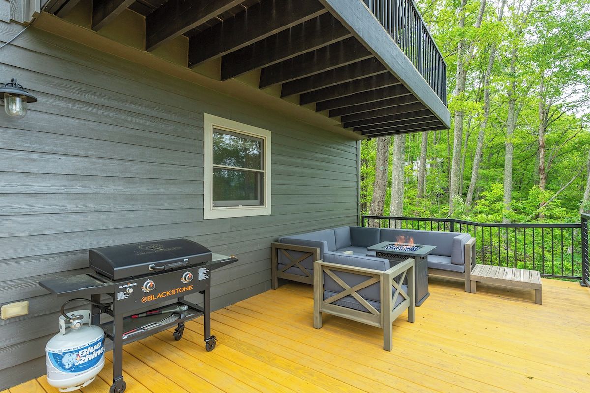 Une terrasse avec un barbecue, des sièges et une vue sur les arbres.