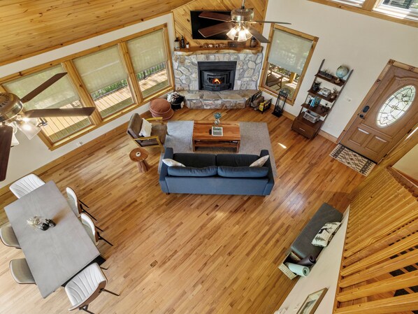 Un amplio espacio de sala de estar con chimenea de piedra, piso de madera, una mesa de comedor con sillas y un sofá.