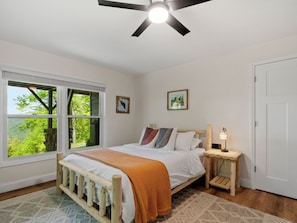 Un dormitorio con cama, ventana, ventilador de techo y mesita de noche.