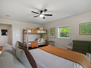 Une chambre avec des lits superposés, un ventilateur de plafond, une fenêtre donnant sur un beau paysage et une commode verte.