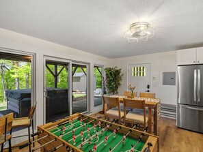 A modern kitchen with a foosball table, a refrigerator, and a dining area with a table and chairs.