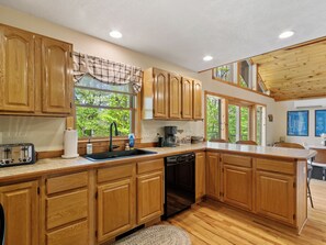 Cocina con armarios de madera, lavavajillas, cafetera y ventana con vistas a árboles.