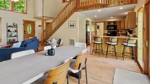 A spacious living area with a dining table, chairs, a staircase, and a kitchen area.