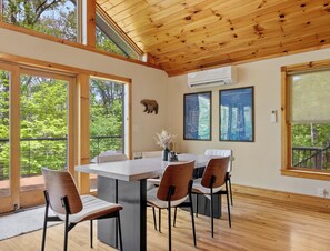 A dining area with a wooden ceiling, large windows, and a view of trees.