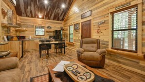 L’intérieur d’un chalet confortable, avec une salle à manger, une cheminée et une grande fenêtre équipée de stores.