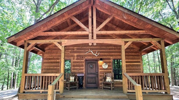 Une cabane en bois avec un porche, des marches menant à l’entrée et une pancarte indiquant « Bienvenue ».