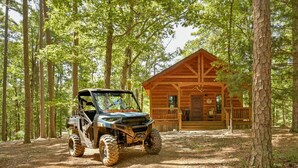 Une cabane au milieu d’une forêt, avec un quad stationné devant.