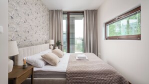 Quarto com cama, mesa de cabeceira, luminária e janela com cortinas.
