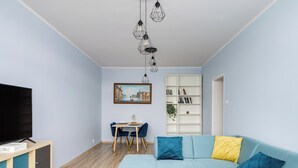 Una sala de estar con un sofá azul claro, un televisor de pantalla plana, un mueble de madera, una mesa de comedor con sillas y una estantería.