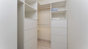 A walk-in closet with multiple shelves and hanging space, featuring a light wood floor and white walls.