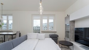 A modern bedroom with a bed, a TV, a dining area, and a window with a city view.