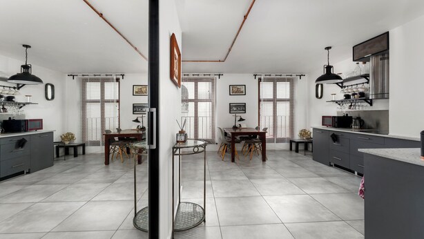 A modern kitchen with a dining area, featuring a central island, dark cabinetry, and a large window with blinds. - Limanowskiego Modern Studio (Kraków)
