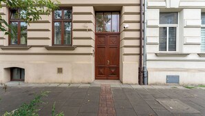 A building facade with a symmetrical design, featuring a central double door with a decorative panel, flanked by windows with brown frames. - Limanowskiego Modern Studio (Kraków)