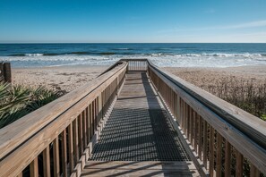 Pasarela de madera que conduce a una playa, con el océano al fondo.