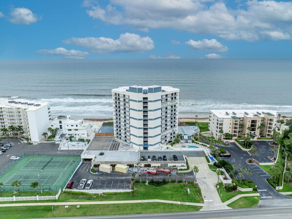 Un hotel frente a la playa con canchas de tenis, estacionamiento y vistas al océano.