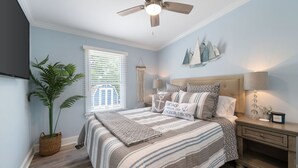 Un dormitorio con cama, mesita de noche, lámpara, planta en maceta y ventilador de techo.