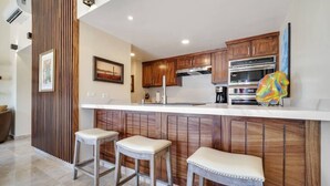 A modern kitchen with wooden cabinets, a white countertop, and two bar stools. - Pedregal, 2 Pools, Quite, Ocean View, Walk to town (Cabo San Lucas)