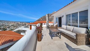A balcony with a sofa, table, and potted plant, overlooking a cityscape. - Pedregal, 2 Pools, Quite, Ocean View, Walk to town (Cabo San Lucas)