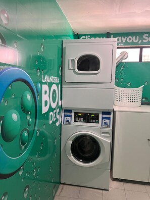 A laundry facility with a front-loading washer and dryer, a wall-mounted microwave, and a basket on the dryer.
