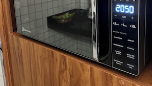 A modern microwave oven with a digital display, wooden cabinet, and a grid-patterned interior.