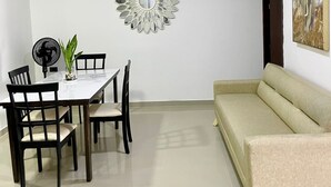 Et spiseområde med et hvidt bord og stole, et dekorativt spejl på væggen og en beige sofa.