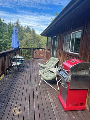 Une terrasse en bois avec un barbecue, des chaises et une table.